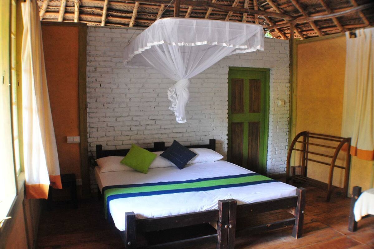 A room with a bed, a green door, a white wall, and a wooden floor.
