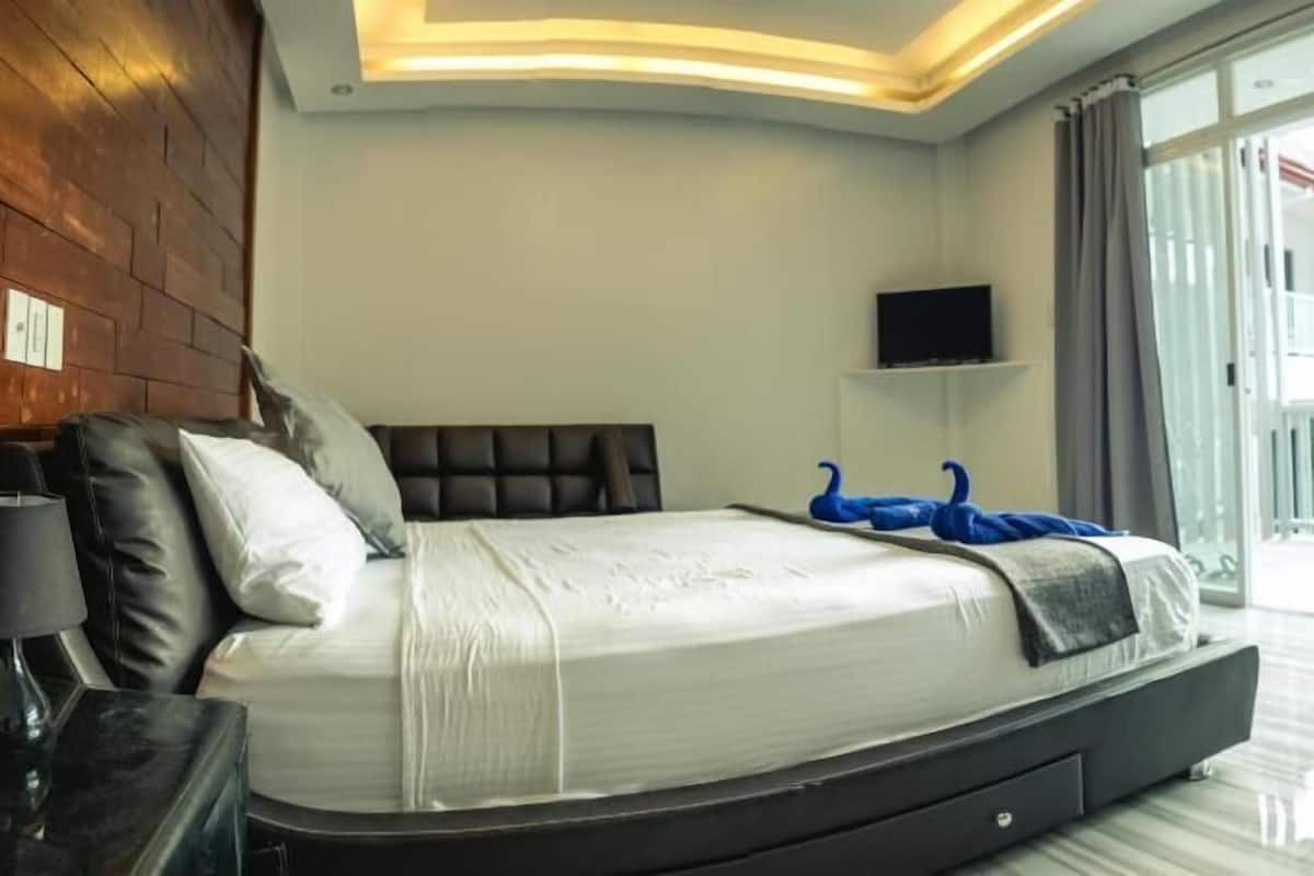 A modern bedroom with a bed, a TV, and a balcony view.