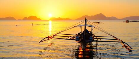 Un barco tradicional con vela, flotando sobre aguas tranquilas al atardecer.