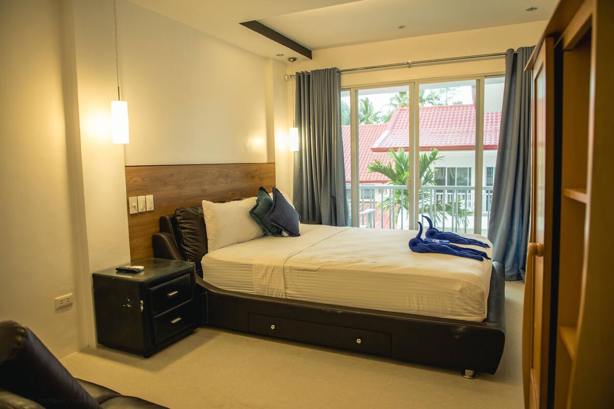 A hotel room with a bed, a nightstand, a chair, and a window with curtains.