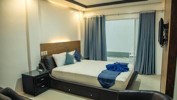 A modern bedroom with a large bed, a nightstand, a chair, and a view of the outdoors through a window with curtains.
