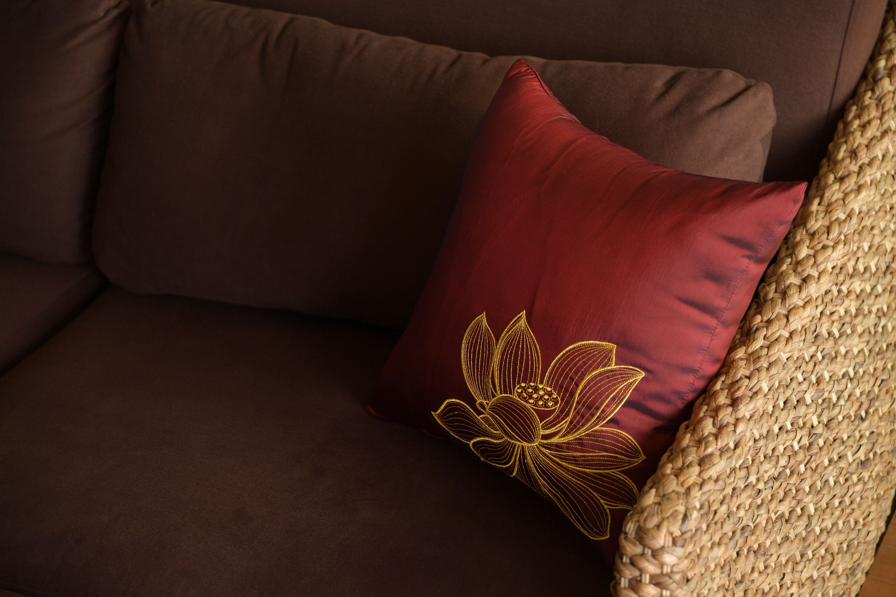 A brown sofa with a red pillow featuring a golden embroidered lotus design.