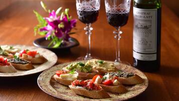Two plates of bruschetta with various toppings, two wine glasses, and a bottle of Chateau Foch-Latt wine on a wooden table.