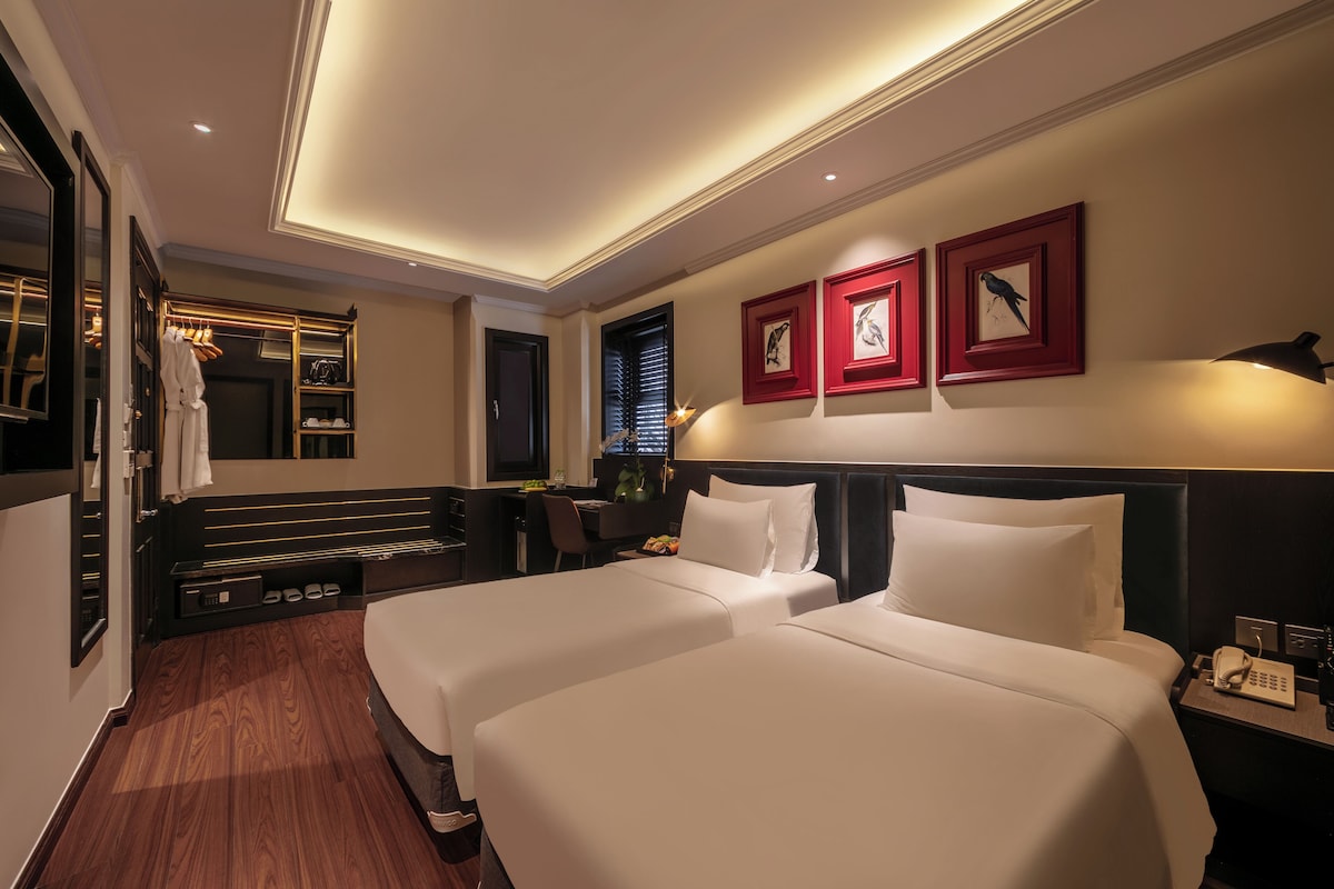 A hotel room with two beds, a desk, a mirror, and a wardrobe.