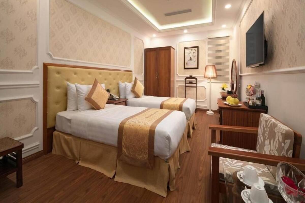 A hotel room with two beds, a desk with a lamp, a television, and a small table with cups.