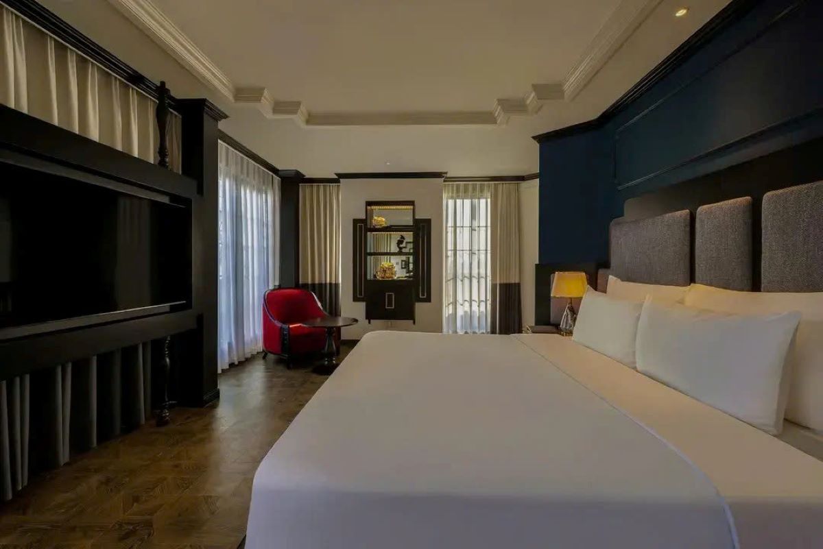 A hotel room with a large bed, a red chair, a television, and a nightstand with a lamp.