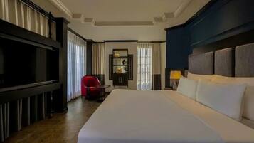 A hotel room with a large bed, a red chair, a television, and a nightstand with a lamp.