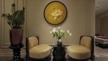 A lobby with two armchairs, a round table with a vase of flowers, and a large framed painting on the wall.