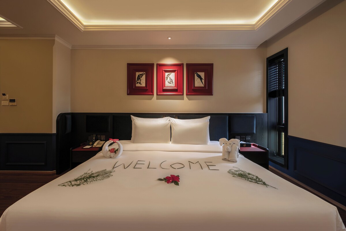 A hotel room with a bed, a nightstand, a telephone, and a window with blinds.