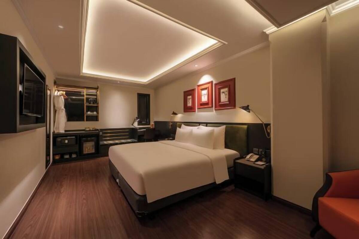 A hotel room with a bed, bedside table, lamp, and a red chair.