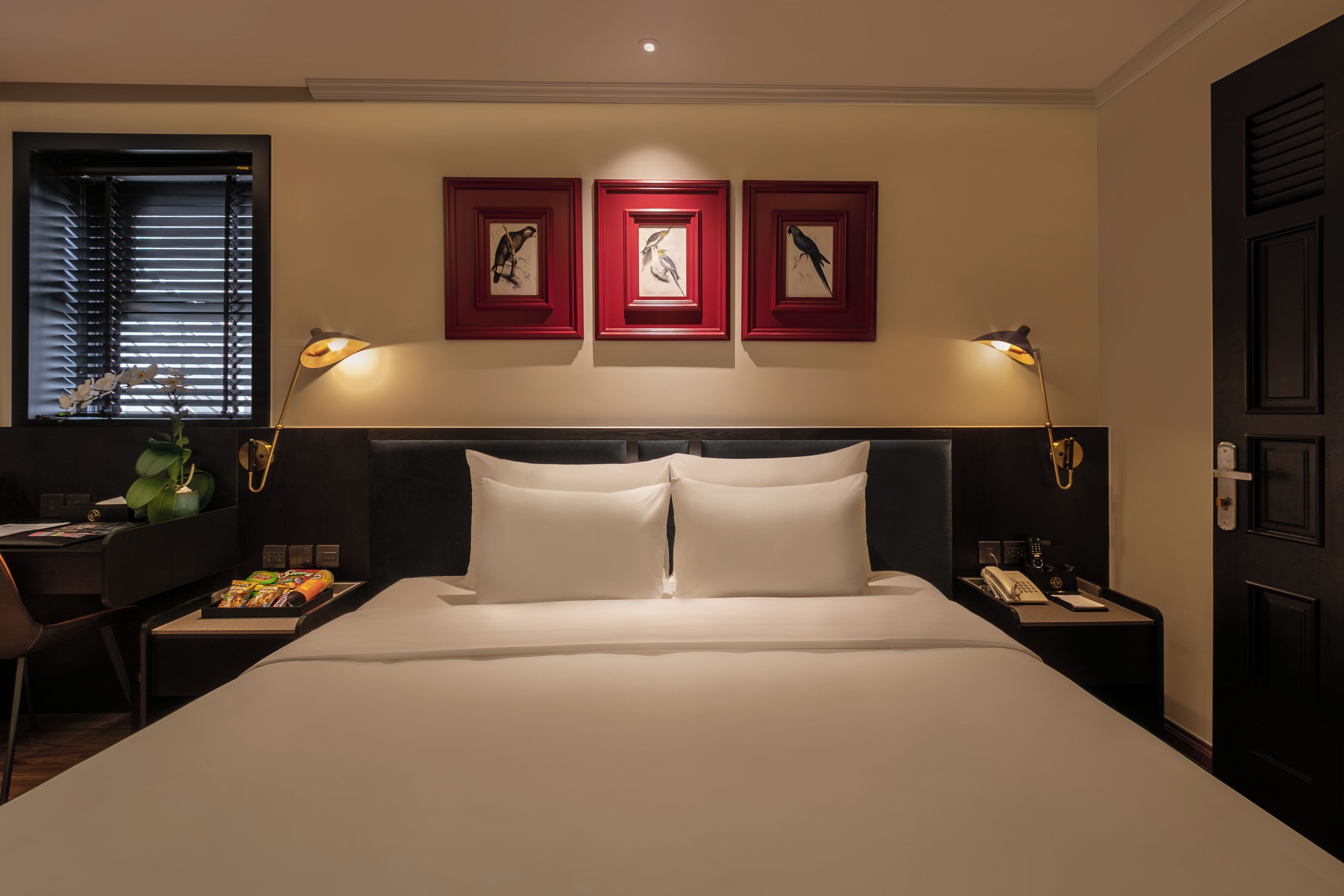 A hotel room with a large bed, two bedside tables, a desk, and a chair. There are framed pictures on the wall above the bed.