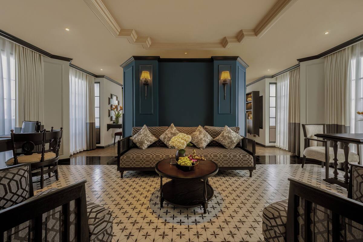 A spacious living room with a patterned floor, a sofa with decorative pillows, a coffee table with a vase, and a dining area with chairs and a table.