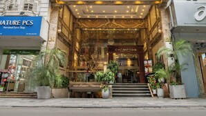 Un hotel con una entrada destacada, un letrero con el nombre y una escalera que conduce a la recepción.