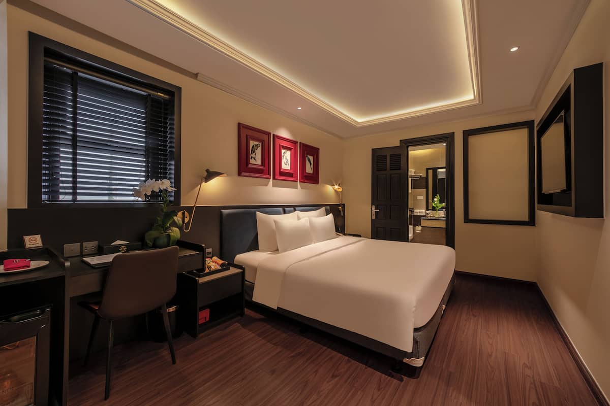 A hotel room with a bed, desk, chair, and bedside table.