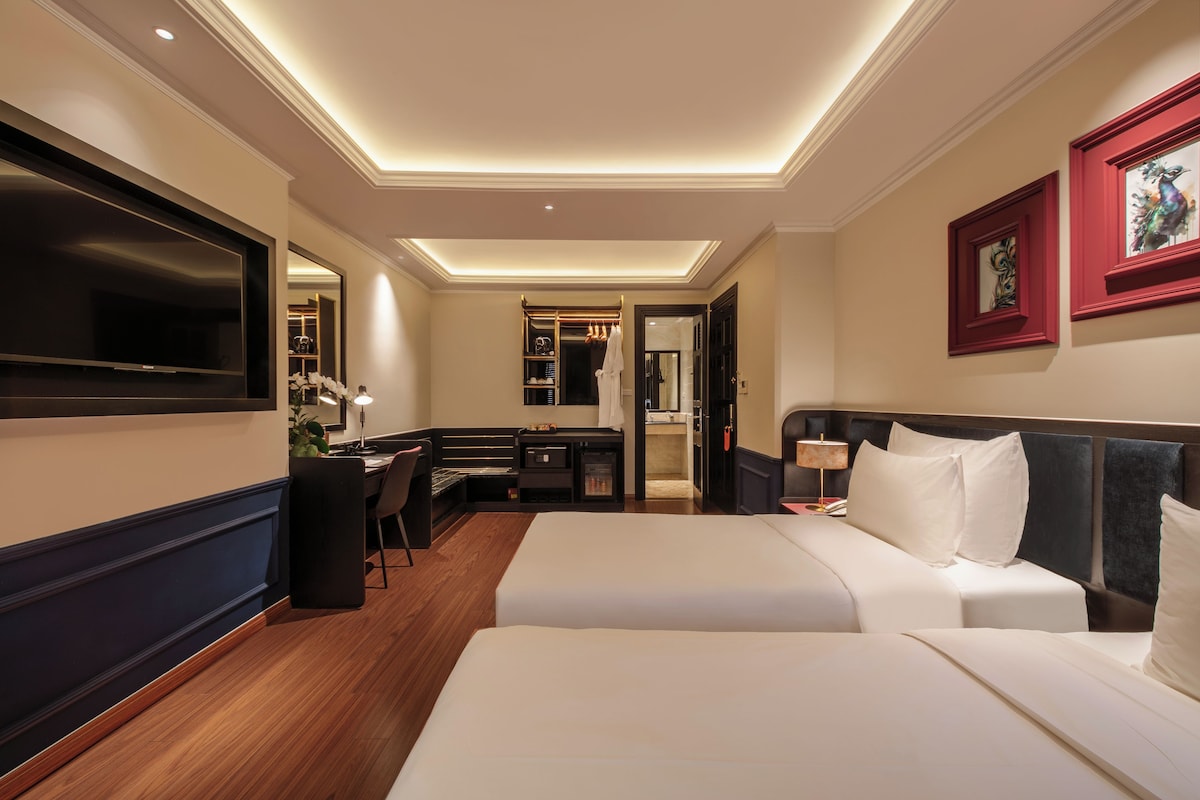 A hotel room with a bed, a desk, a chair, a TV, and a bathroom visible through an open door.
