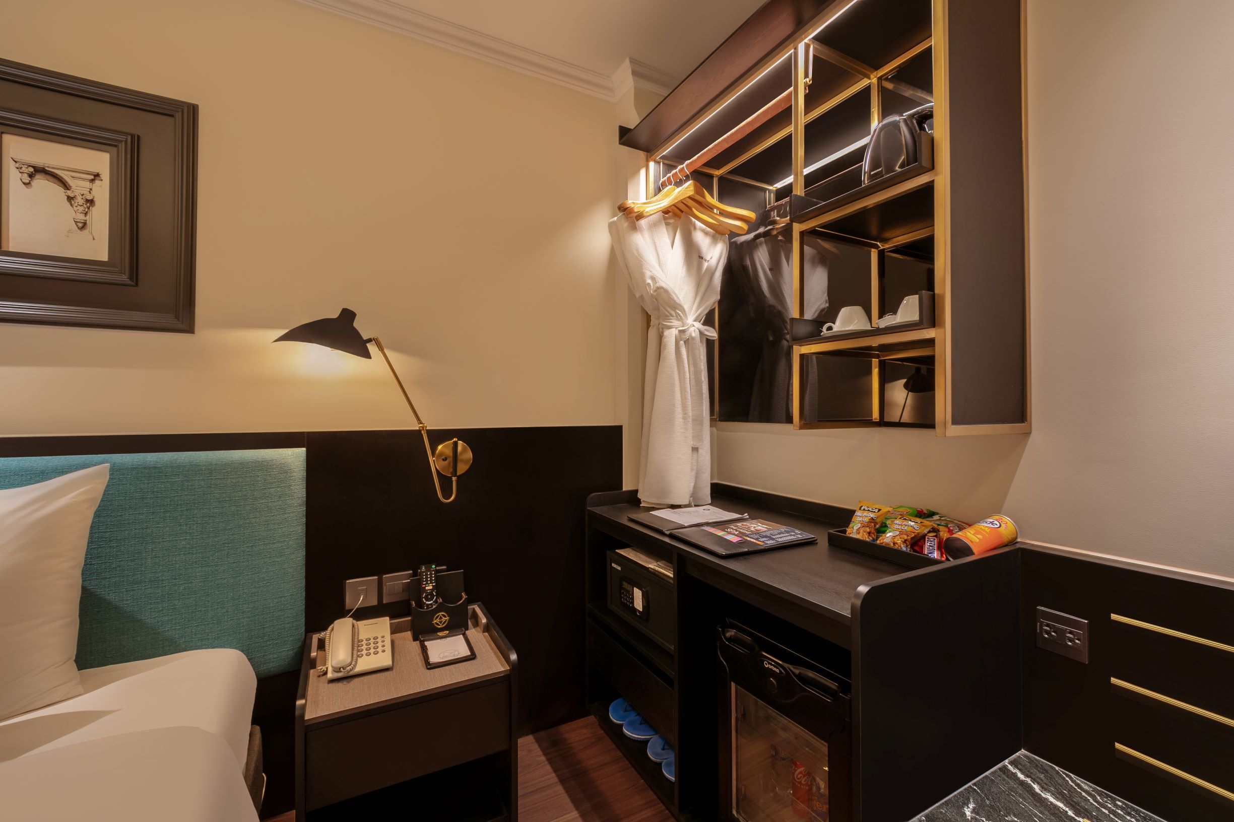 A hotel room with a bed, a desk with a telephone, a mirror, and a minibar.