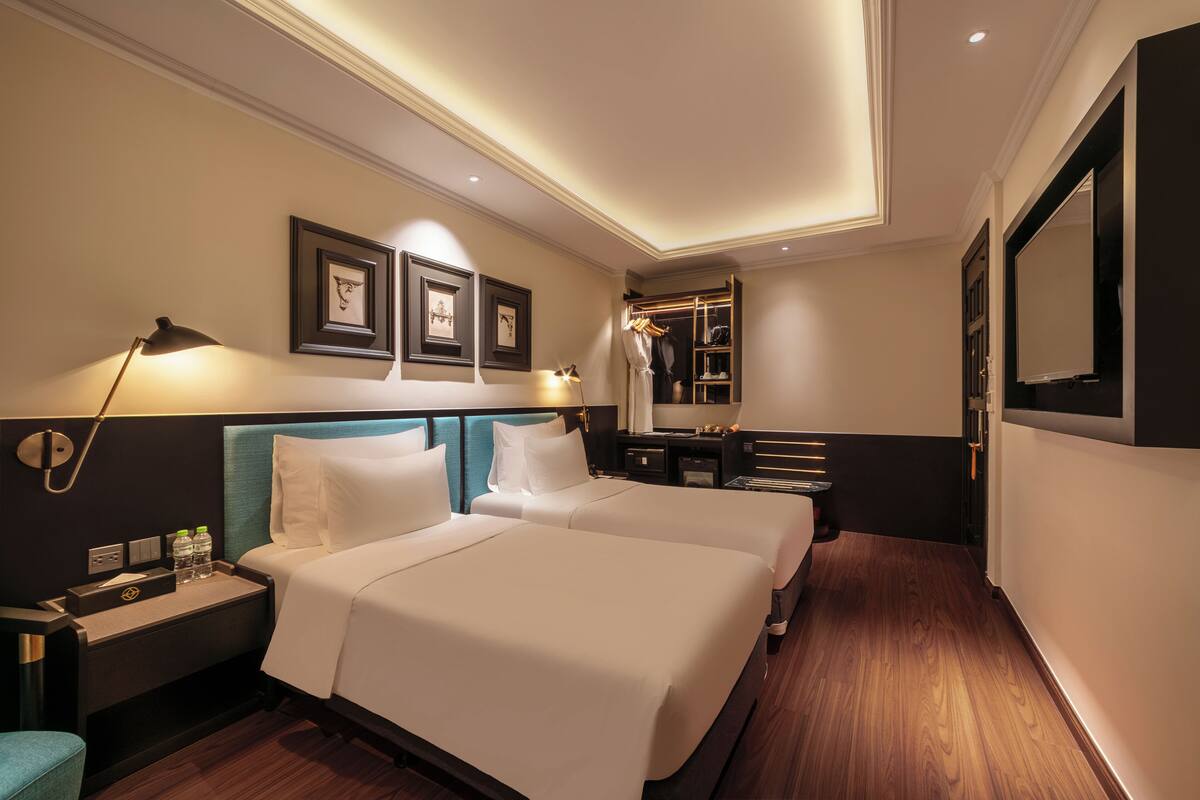 A hotel room with two beds, a nightstand, a desk, a mirror, and a wardrobe.