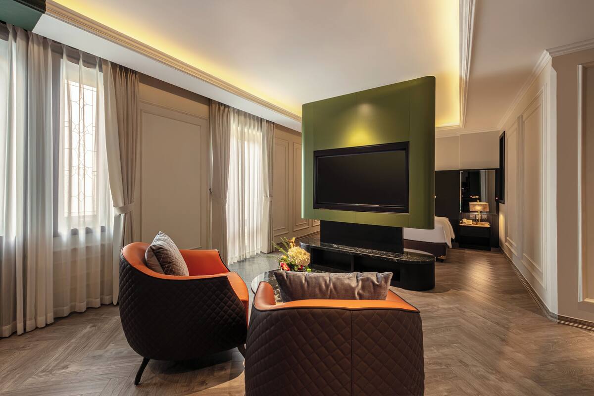 A modern living room with a flat-screen TV, two upholstered chairs, a coffee table, and a decorative vase.