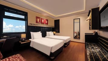 A hotel room with two beds, a desk, a chair, a TV, and a large window.