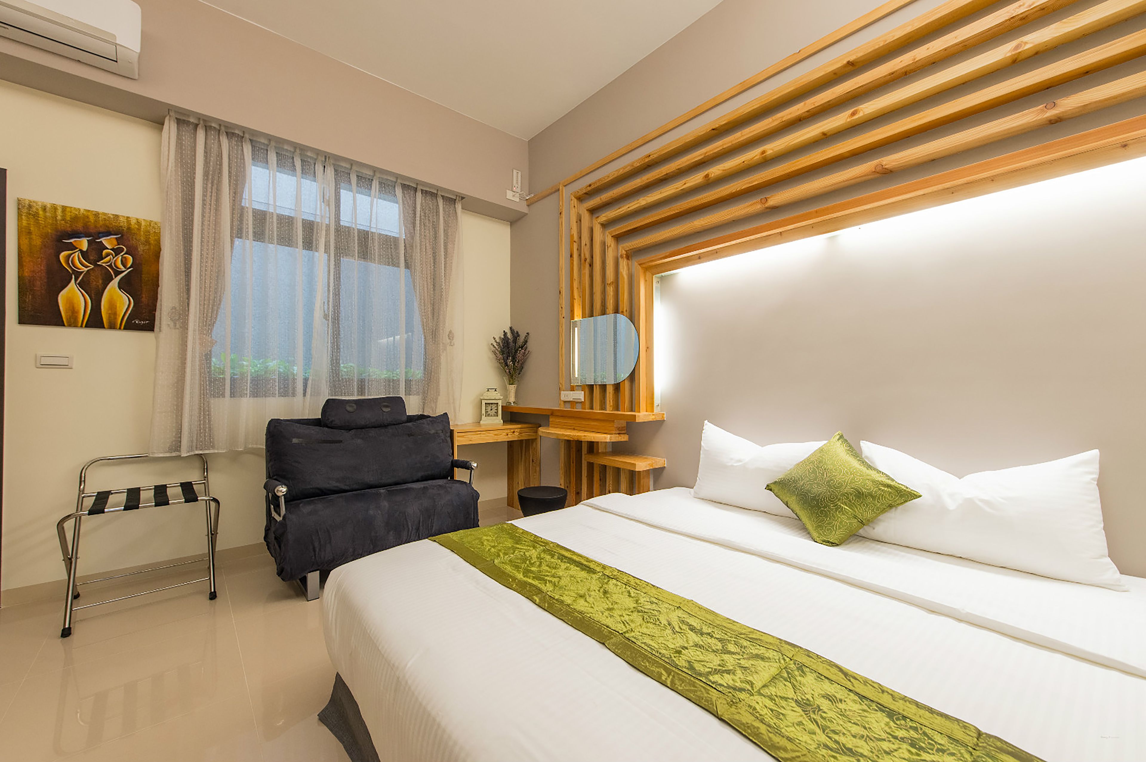 Une chambre d’hôtel comprenant un lit, un bureau, une chaise, une petite table, un miroir et une fenêtre avec des rideaux.
