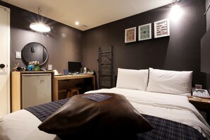 A hotel room with a bed, a desk with a computer, a small refrigerator, a mirror, and a wall-mounted phone. - Kotel Sinchon (Seoul)