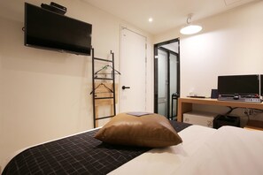 A hotel room with a bed, a TV mounted on the wall, a desk with a computer, and a door leading to a bathroom. - Kotel Sinchon (Seoul)