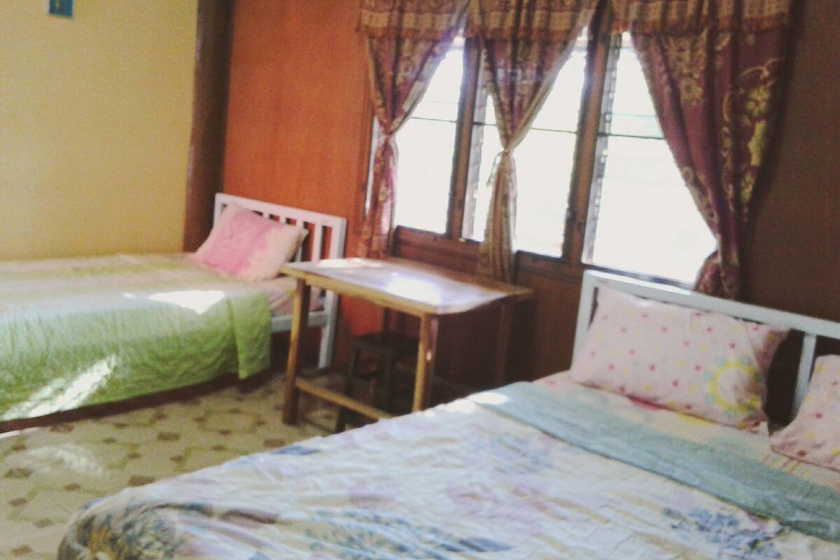 A room with two single beds, a small table, and a window with curtains.