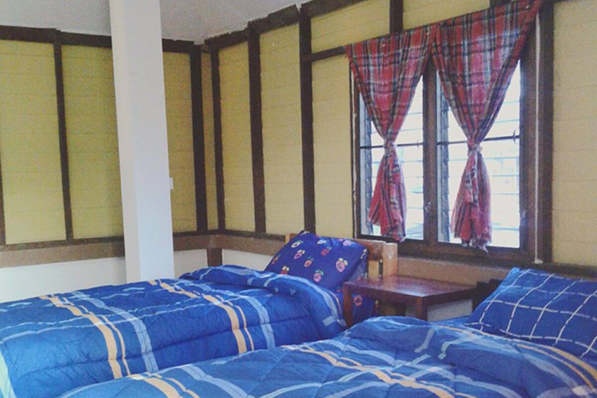 A room with two beds, a window with plaid curtains, and a wooden ceiling.