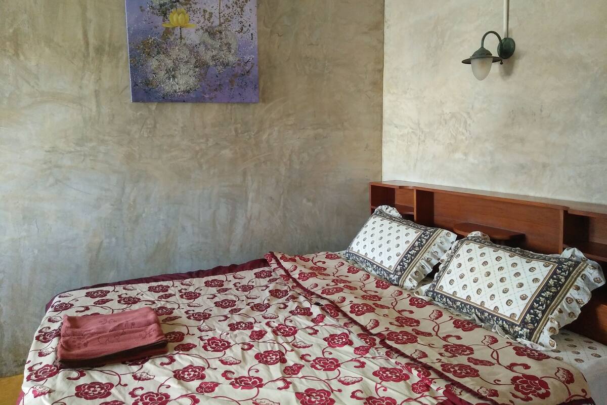 A bedroom with a bed, pillows, and a painting on the wall.
