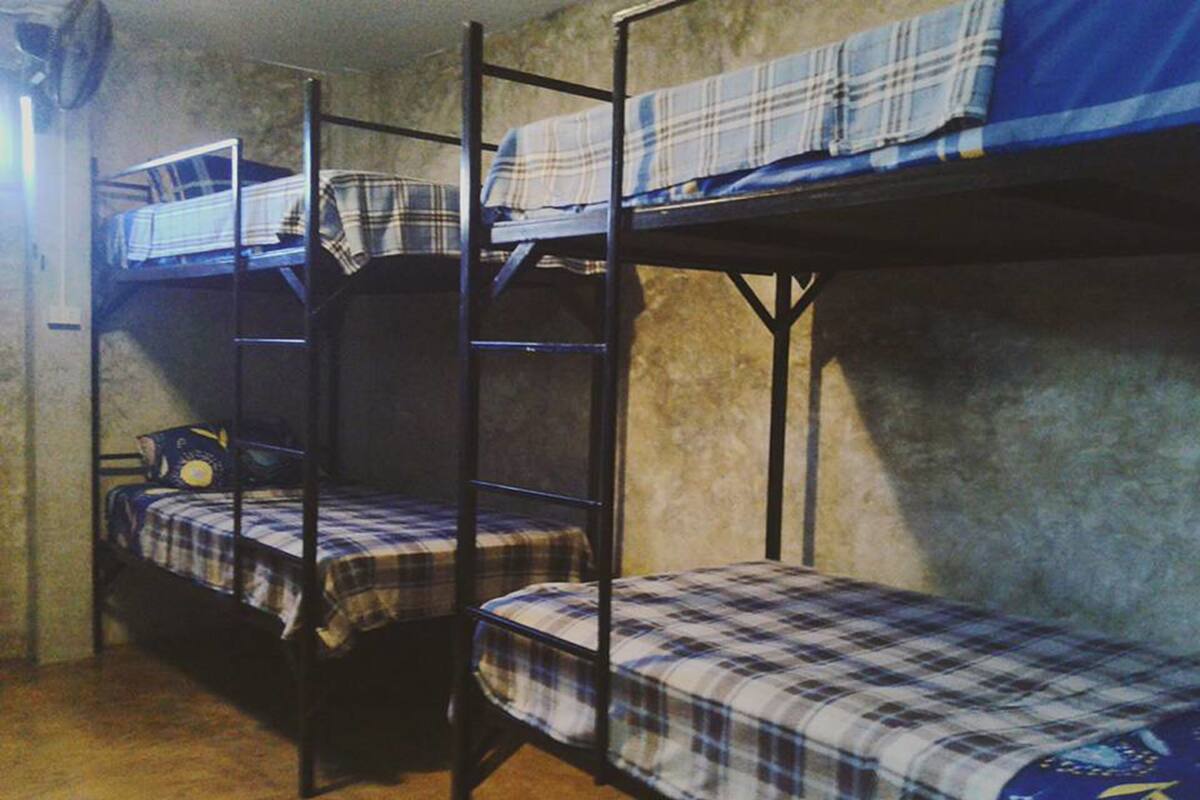 A dormitory room with bunk beds, a fan, and a small table with a chair.