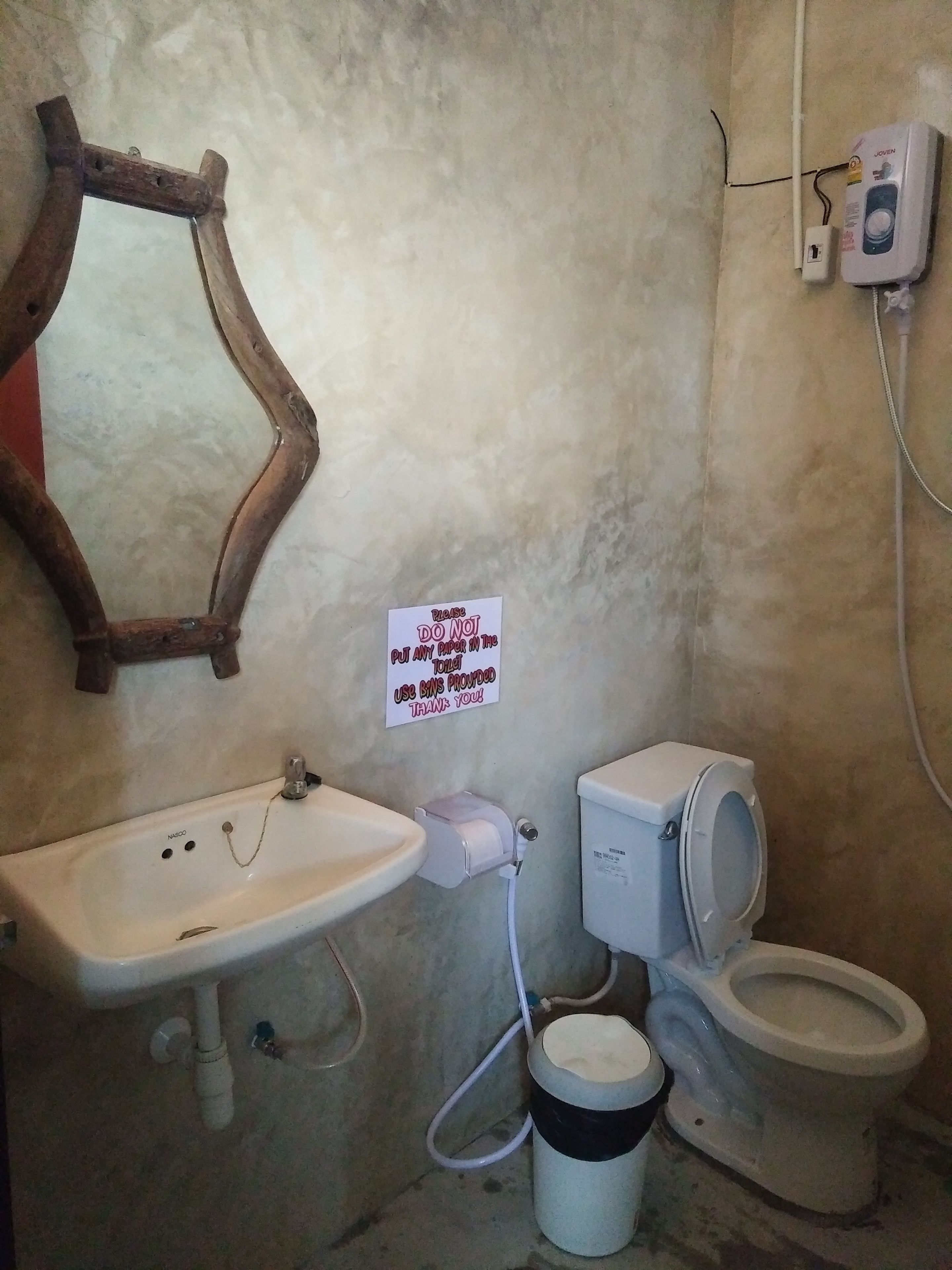 A bathroom with a sink, toilet, and a mirror. There is a sign on the wall instructing to use bins provided.