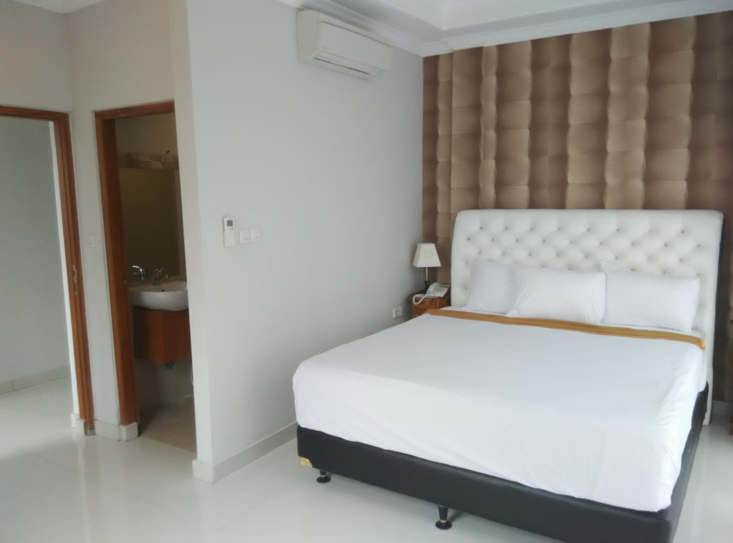 A hotel room with a large bed, a bedside table with a lamp, and a wall-mounted air conditioner.