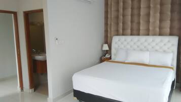 A hotel room with a large bed, a bedside table with a lamp, and a wall-mounted air conditioner.