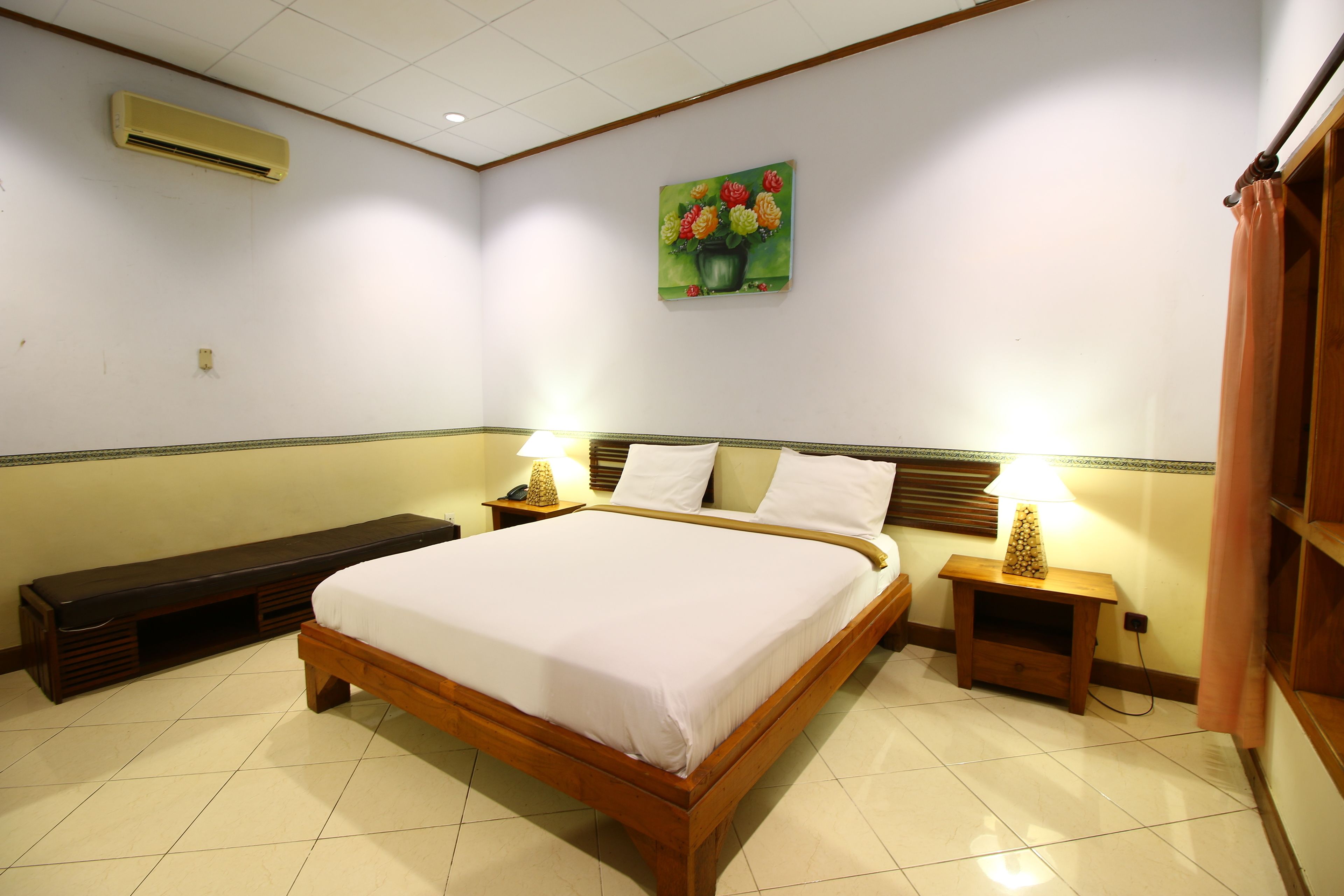 Un dormitorio con una cama de madera, dos mesitas de noche con lámparas, un banco y un aire acondicionado instalado en la pared.