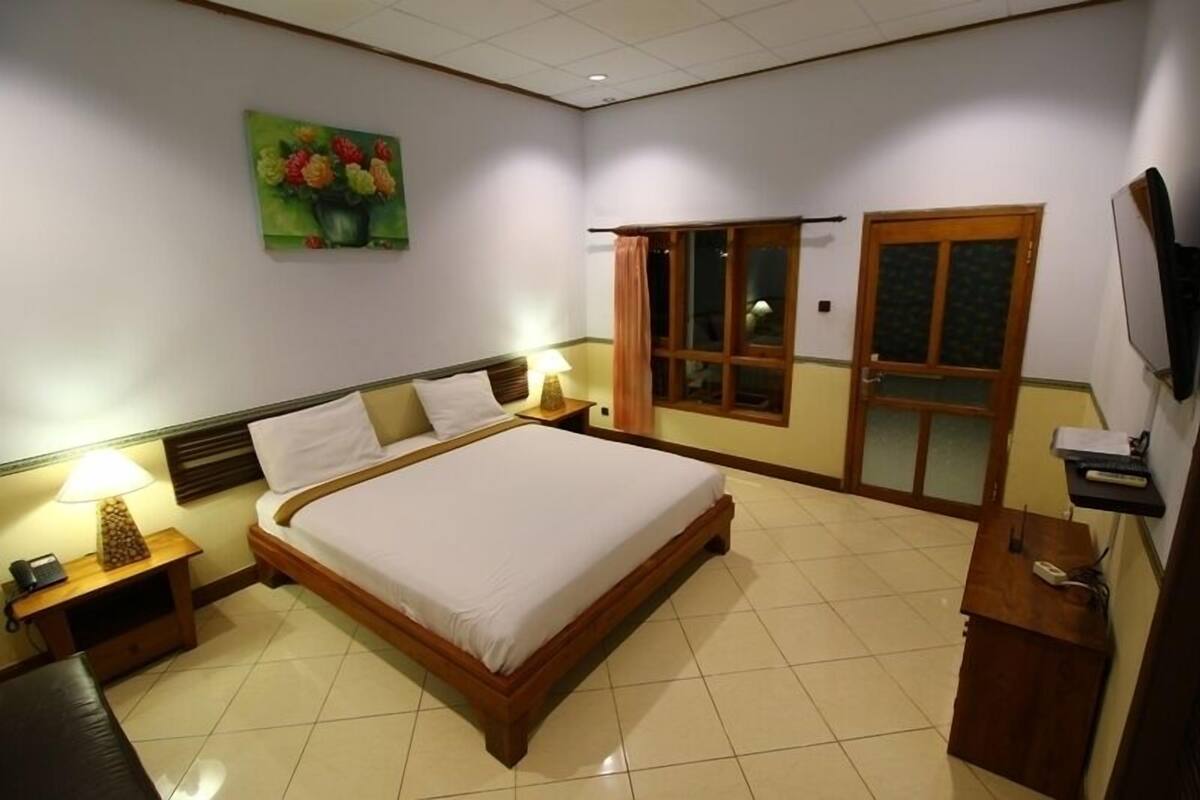 Une chambre d’hôtel avec un lit, des tables de chevet, un bureau, une télévision et une fenêtre avec des rideaux.