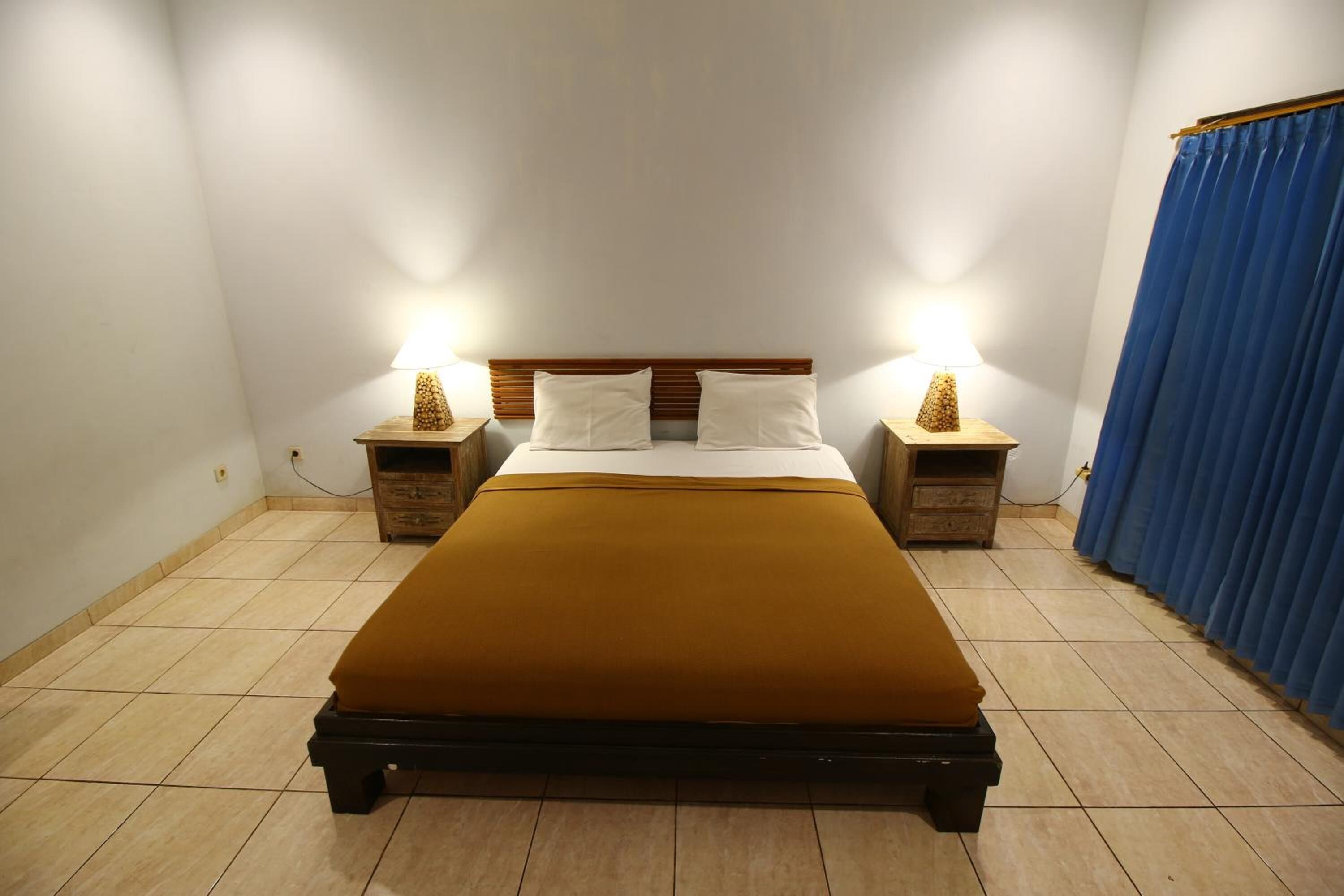 A neatly made bed with a brown bedspread, two bedside tables with lamps, and a blue curtain on the right.