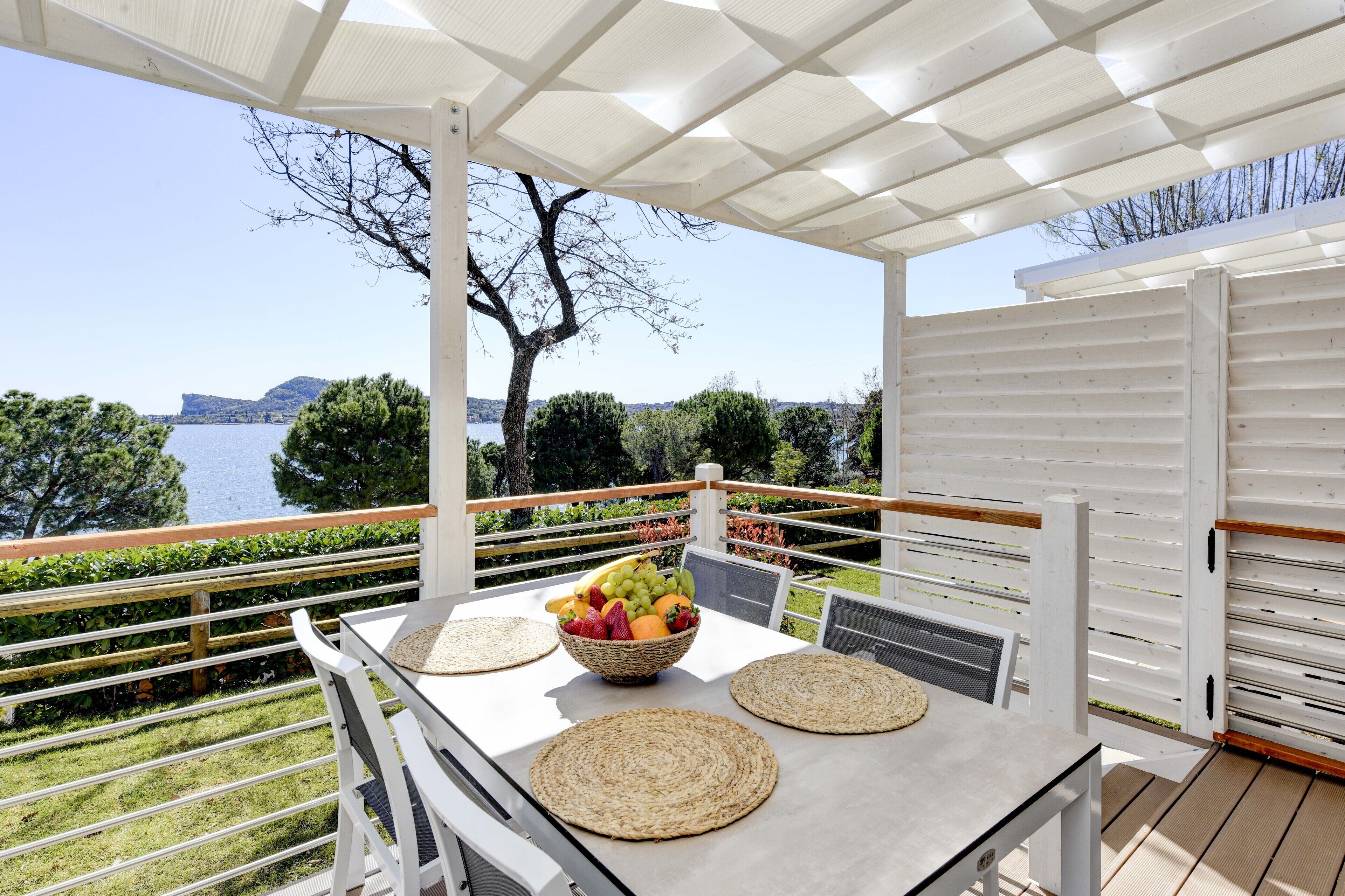 Un espacio exterior techado con comedor, una mesa preparada para dos, un frutero y vistas al mar y las colinas.