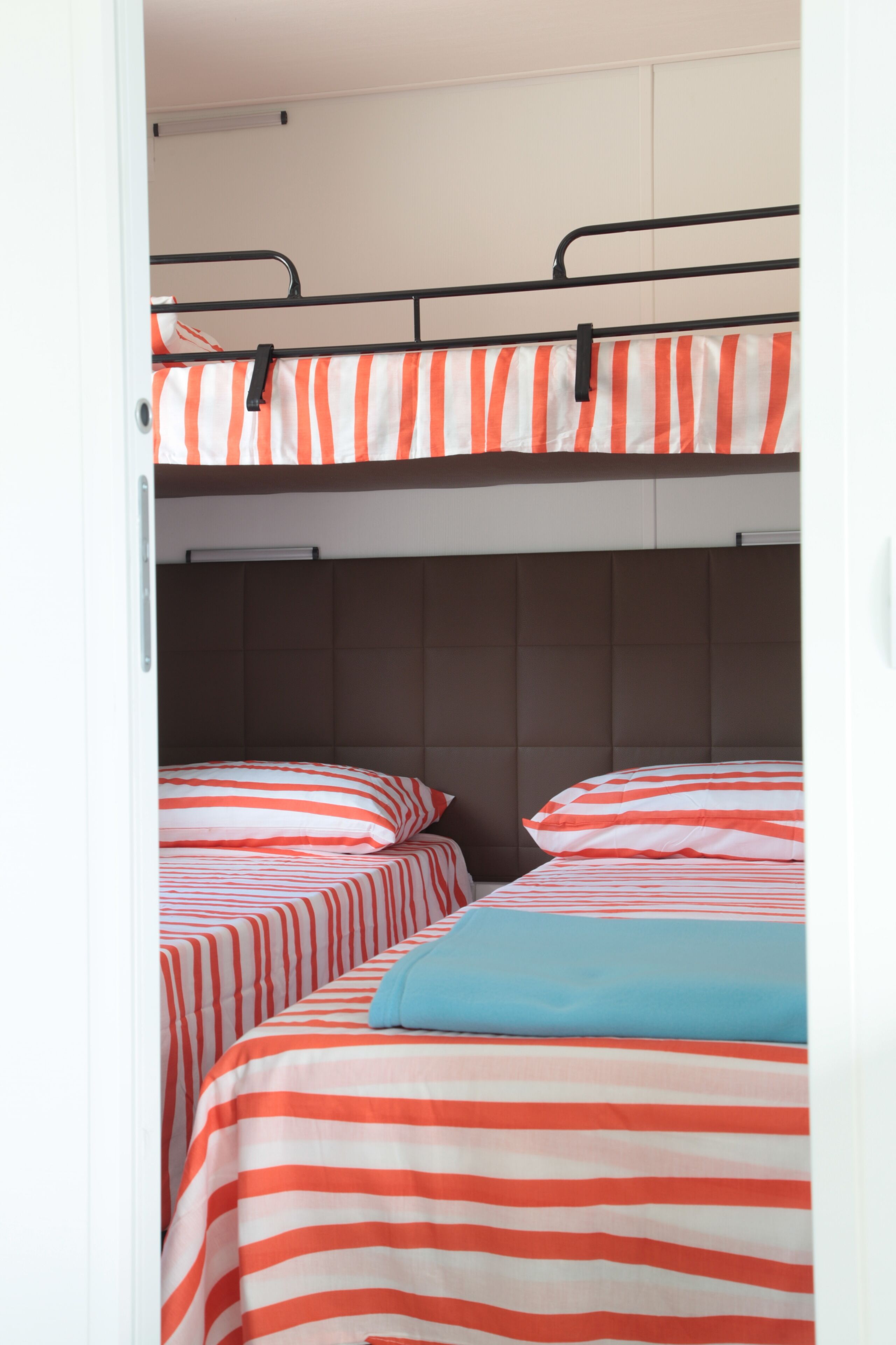 Een slaapkamer met stapelbedden, gestreept beddengoed en een hoofdbord.