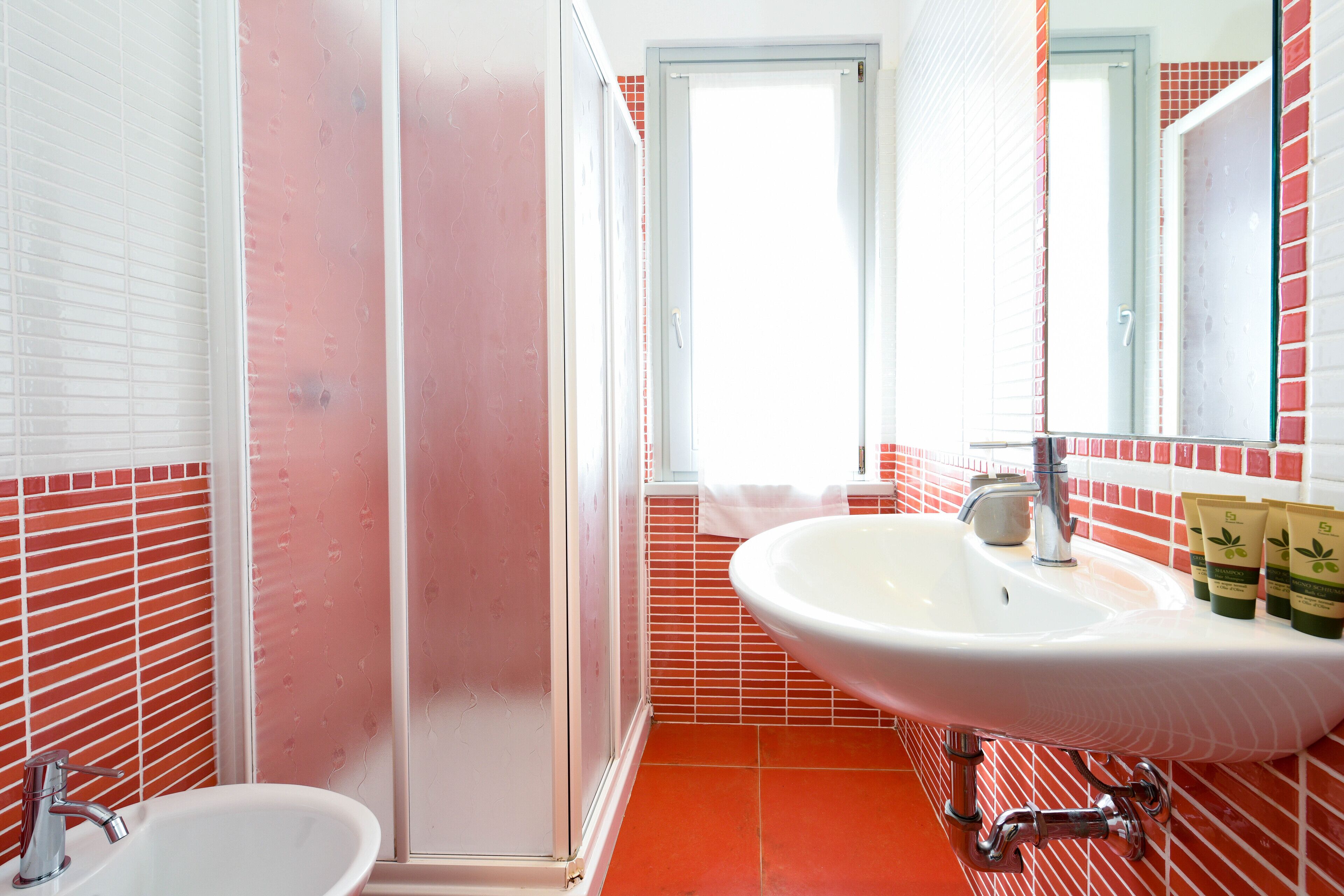 A bathroom with a white sink, a mirror, and red-tiled walls.