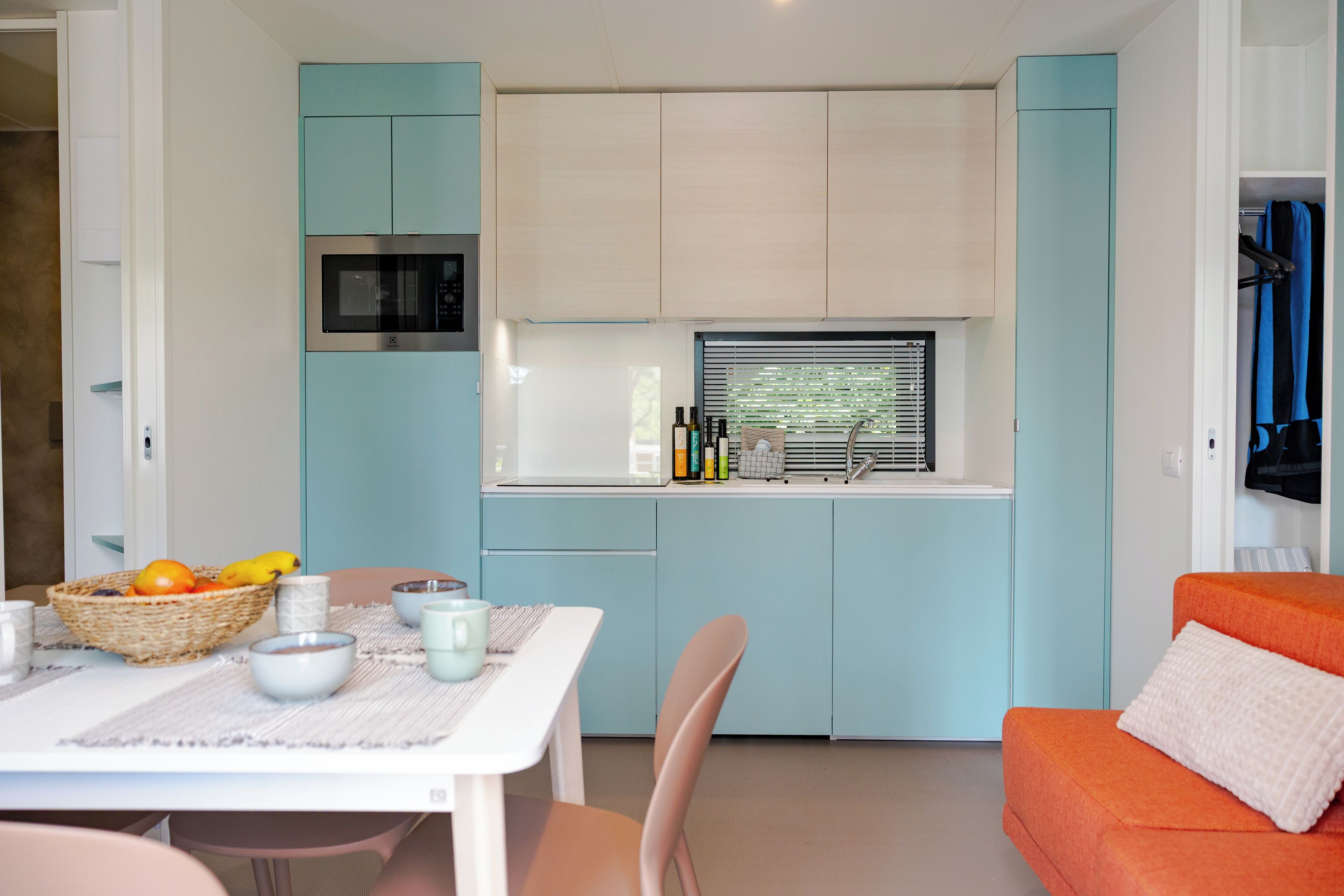 A compact kitchen with teal cabinetry, a microwave, and a window with blinds.