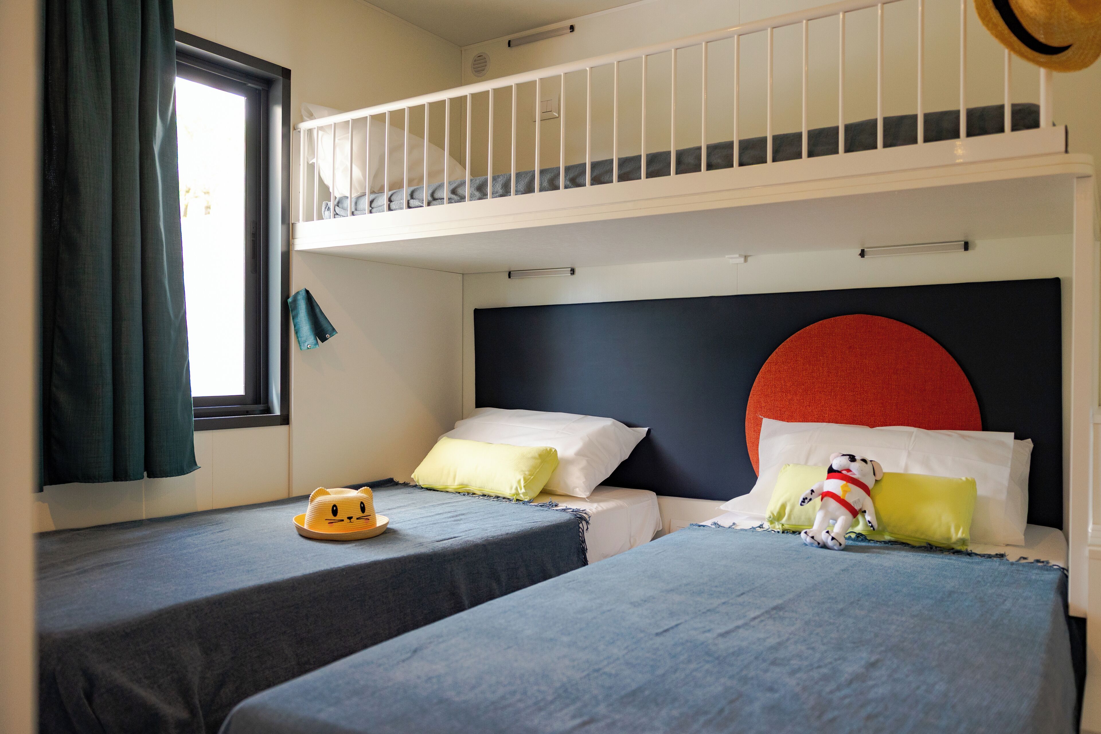Una habitación con dos camas individuales, una ventana con cortinas, una mesita con un sombrero y un ventilador de techo.