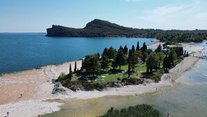 A coastal area with a beach, a small hill with trees, and a clear view of the sea. - Camping Europa Silvella (Manerba del Garda)