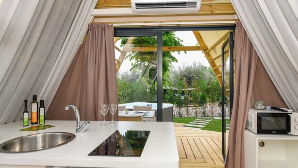 A compact kitchenette with a sink, faucet, and microwave, a dining area with a table and chairs, and a sliding glass door leading to an outdoor patio. - Camping Europa Silvella (Manerba del Garda)
