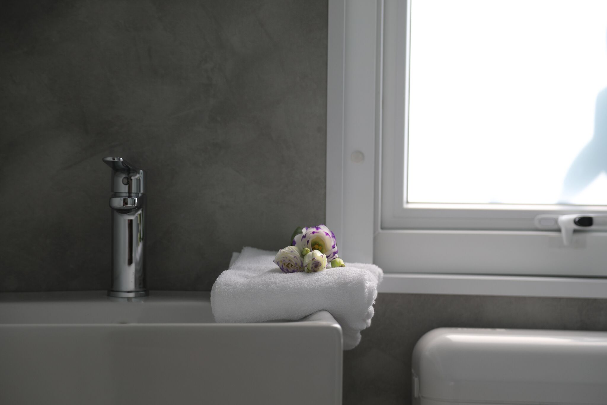 Bagno con vasca da bagno bianca, un rubinetto e una finestra con vista su una persona all'esterno.