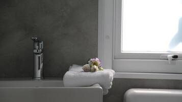 Bagno con vasca da bagno bianca, un rubinetto e una finestra con vista su una persona all'esterno.