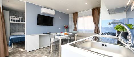 A compact hotel room with a kitchenette, a dining area, and a sleeping area with a bunk bed.