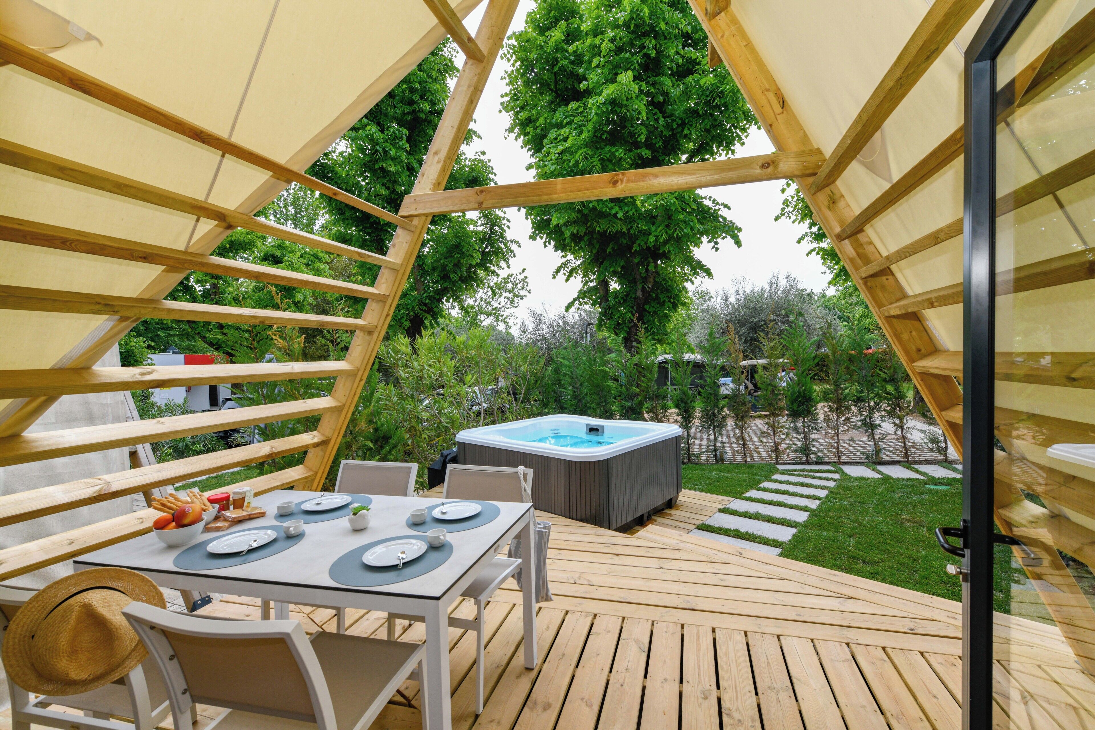 An outdoor dining area with a table set for four, surrounded by wooden deck and a hot tub.