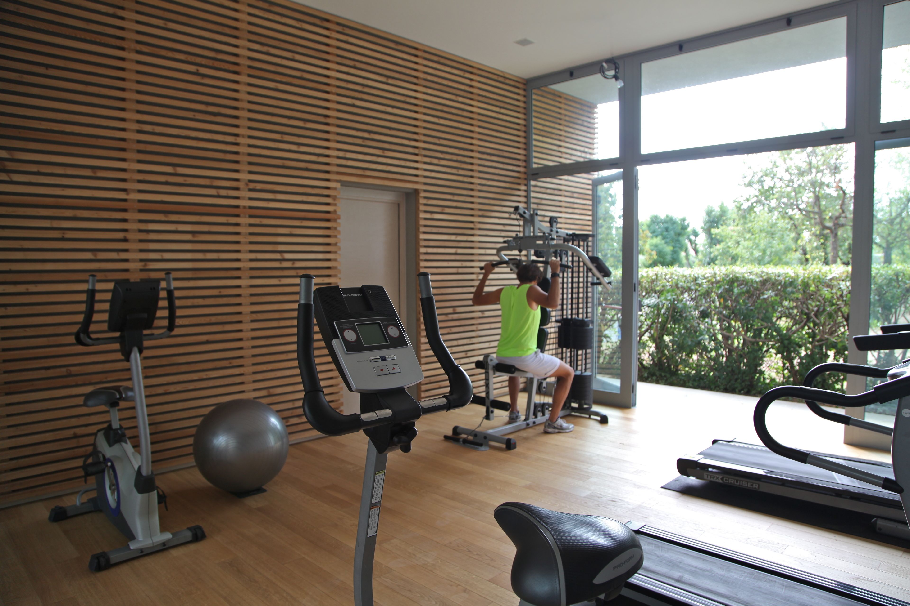 A gym with exercise equipment, large windows, and a wooden wall.