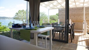 A dining area with a table set for two, overlooking a body of water, with a wooden deck and a covered seating area. - Camping Europa Silvella (Manerba del Garda)
