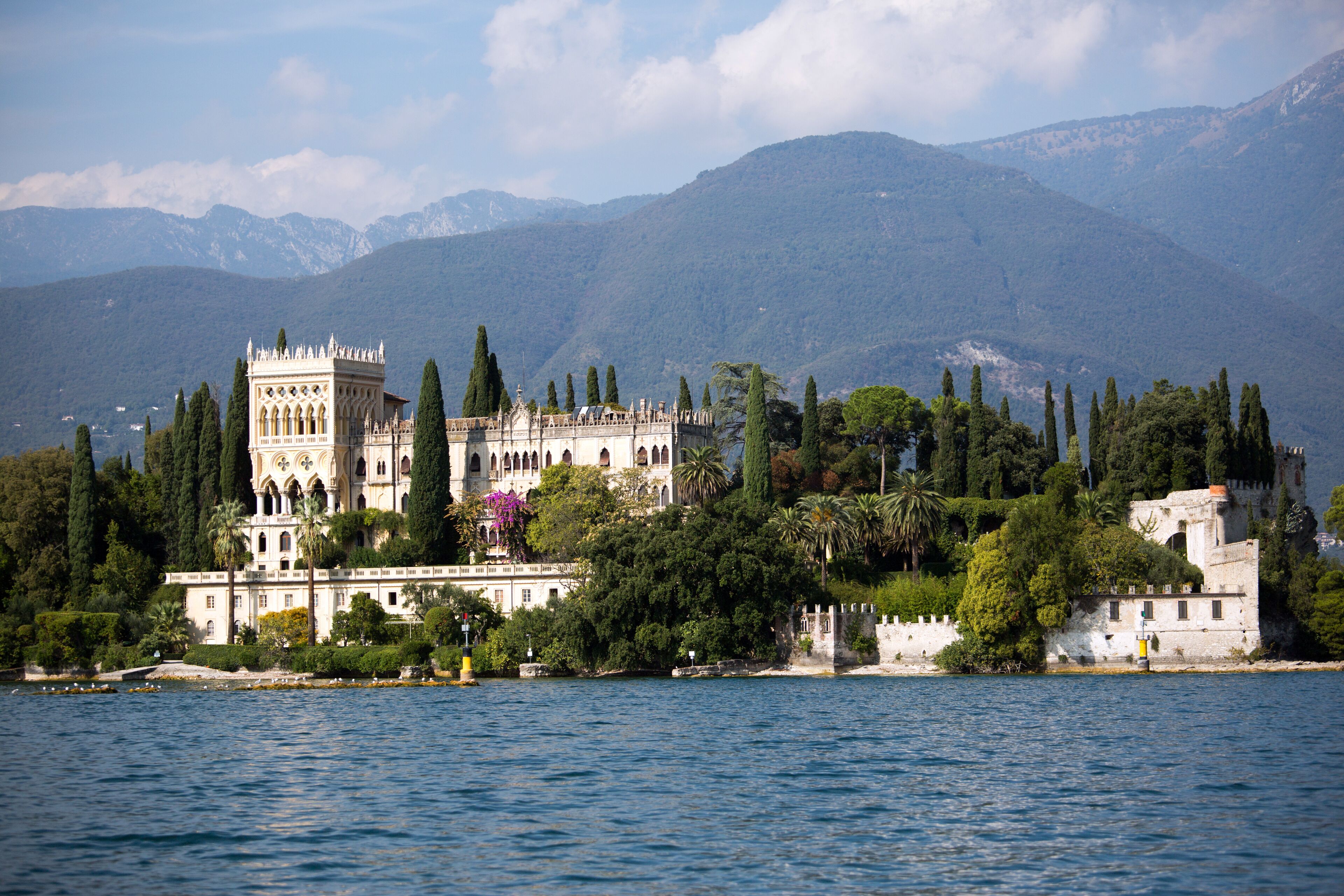 A historic building with a tower, surrounded by trees and mountains in the background.